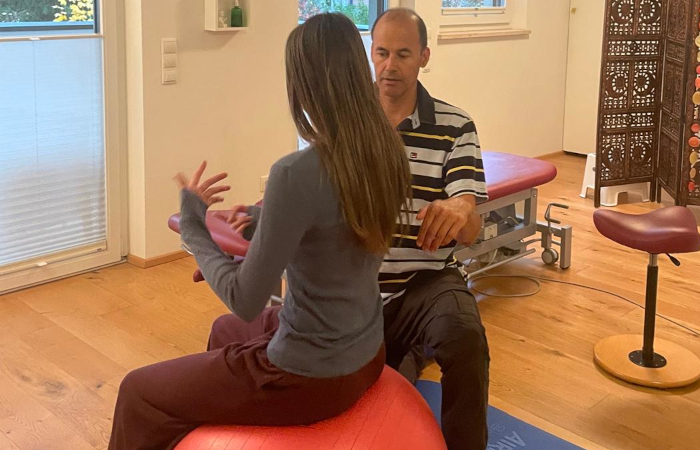 Roland bespricht eine Übung mit einer Patientin, die auf einem Gymnastikball sitzt.